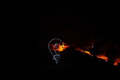 Light trails on illuminated fire against sky at night