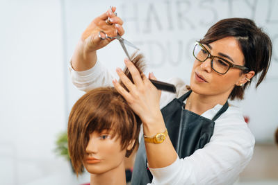 Hairdresser educator with students, explaining hair cutting technique on mannequin head for training