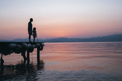 Italy, lazise, father and little daughter standing on jetty looking at lake garda at sunset