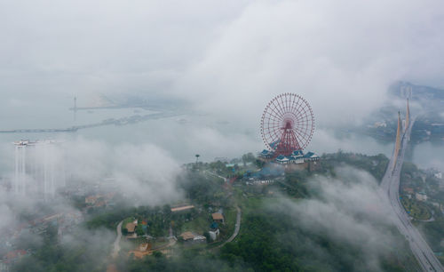 Aerial view of ferris wheel and bridge in city during foggy weather