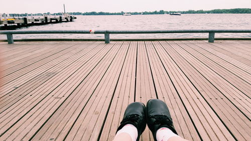 Low section of person relaxing on pier over river