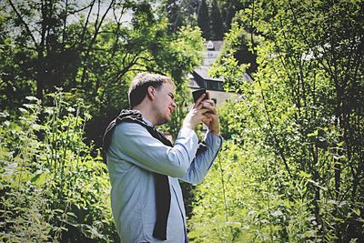 Side view of man photographing through mobile phone by plants