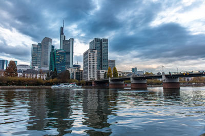 Buildings by river against cloudy sky