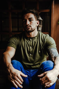 Portrait of young man sitting by plant indoors