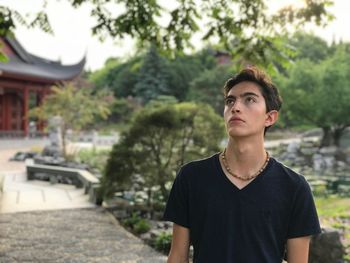 Portrait of young man looking away against trees