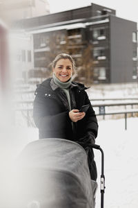 Smiling woman with pram holding cell phone