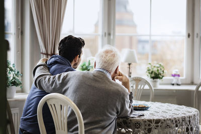 Rear view of man sitting with arm around caretaker at nursing home