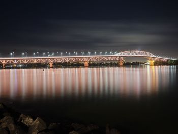 Illuminated bridge over river against sky at night