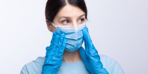 Doctor in mask wearing surgical glove looking away against gray background