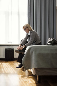 Side view of businesswoman tying shoelace sitting on bed at hotel room