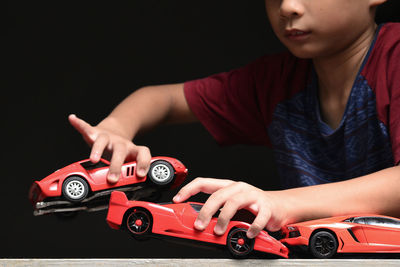 Midsection of boy playing with toy cars against black background