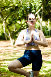 Young woman meditating while standing against trees at park