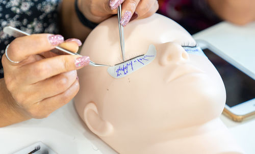 Cropped image of woman applying eyelash on mannequin