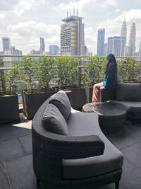 Man sitting on chair against modern buildings in city