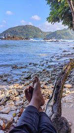 Low section of man relaxing at beach against sky