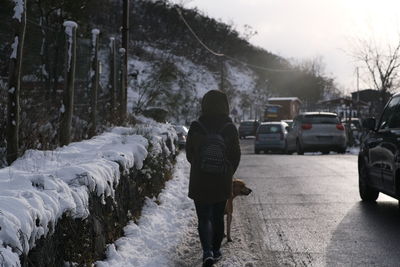 Rear view of woman and dog walking on snow covered landscape