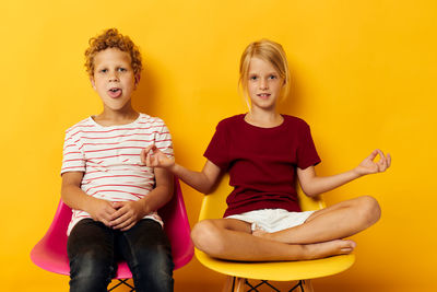 Portrait of siblings sitting on sofa against yellow background