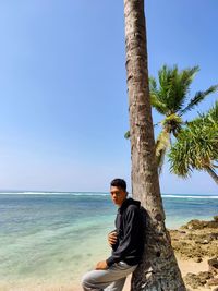 Young man sitting on shore at beach against sky