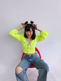 Portrait of asian woman in chartreuse top sitting in a red chairover white background