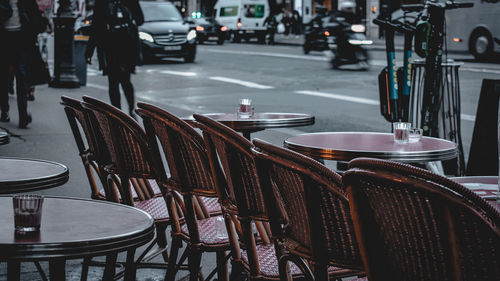 Empty chairs and tables at sidewalk cafe in city