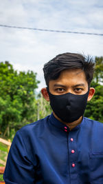 Portrait of man wearing mask standing outdoors against sky