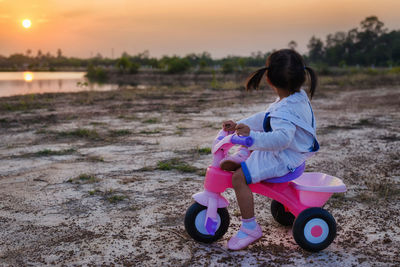 Full length of girl on tricycle at beach against sky during sunset