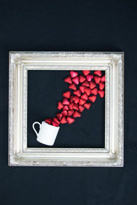 Directly above shot of red heart shapes and cup in picture frame on black background