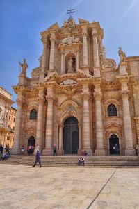 People in facade of historic building against sky