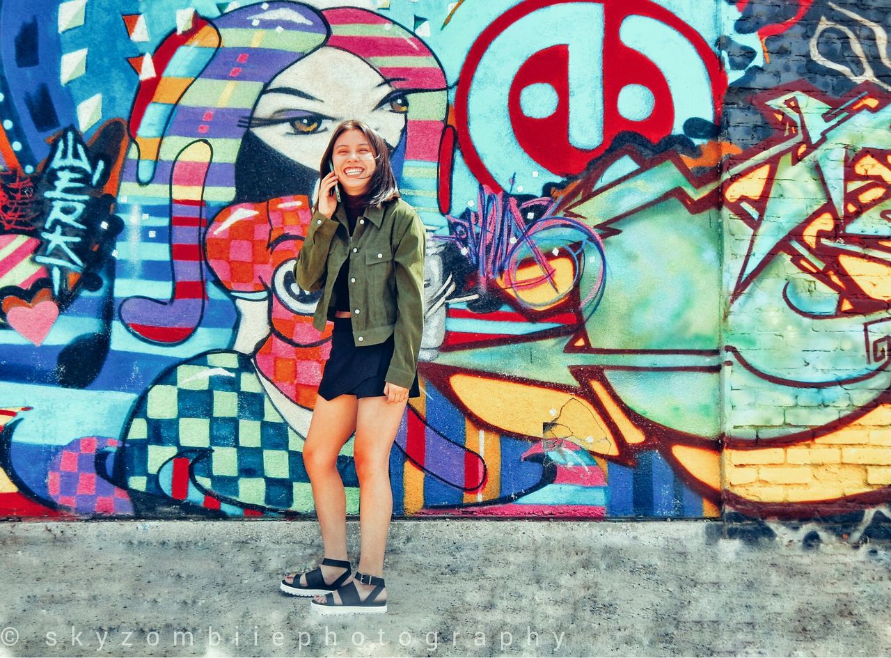 graffiti, art, creativity, art and craft, wall - building feature, architecture, built structure, multi colored, lifestyles, human representation, casual clothing, standing, building exterior, wall, young adult, front view, full length, leisure activity