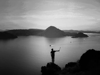 Silhouette man taking selfie while standing on rock against river during sunset