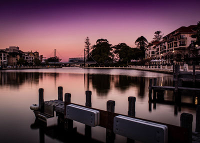 River by illuminated buildings against sky at sunset