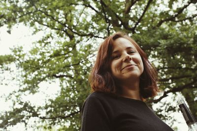 Low angle portrait of young woman standing against tree