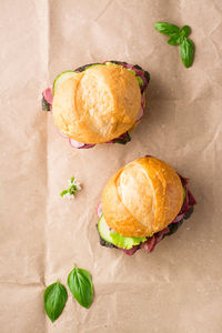 A couple of fresh burgers with pastrami, cucumber, radish and herbs on craft paper