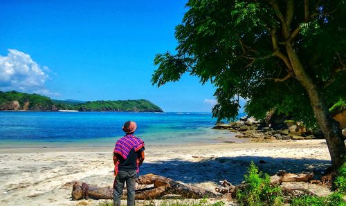 Rear view of woman sitting on beach against sky