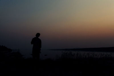 Silhouette man standing on shore during sunset