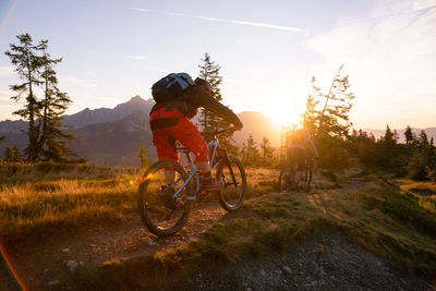 People riding bicycle on field against sky during sunset