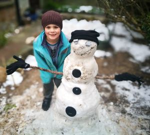 Portrait of boy standing by snowman