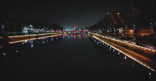 Illuminated bridge over river by buildings in city at night