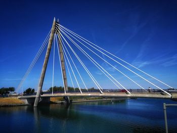 Low angle view of suspension bridge over river against blue sky