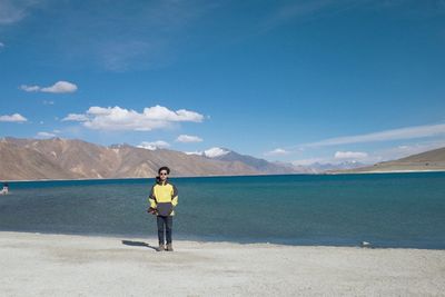 Rear view of man standing on shore against blue sky