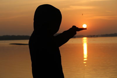 Silhouette boy standing on beach against sky during sunset