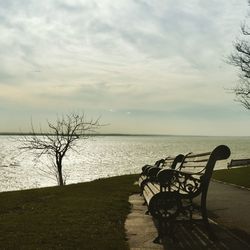 Bench by sea against sky