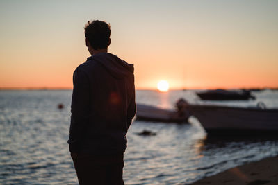 Rear view of silhouette man standing at beach during sunset