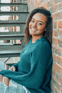 Portrait of smiling young woman sitting against wall