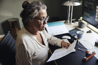 Mature female freelancer examining documents at desk in home office