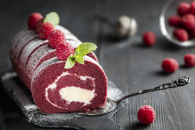 Red velvet sponge swiss roll with fresh raspberry and sugar icing on dark background