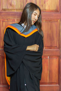 Thoughtful young woman in graduation gown standing door