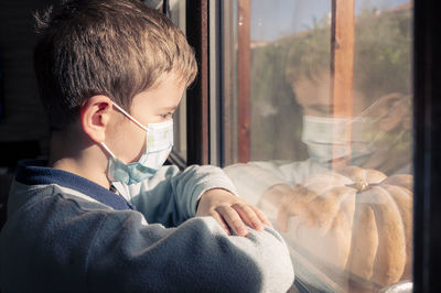 Illness child on home quarantine. boy wear protective medical masks sits on windowsill