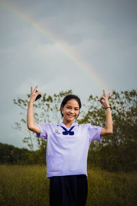 Portrait of smiling teenage girl showing peace sign on grassy field