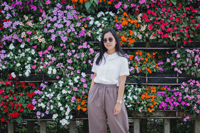 Portrait of young woman standing against flowering plants